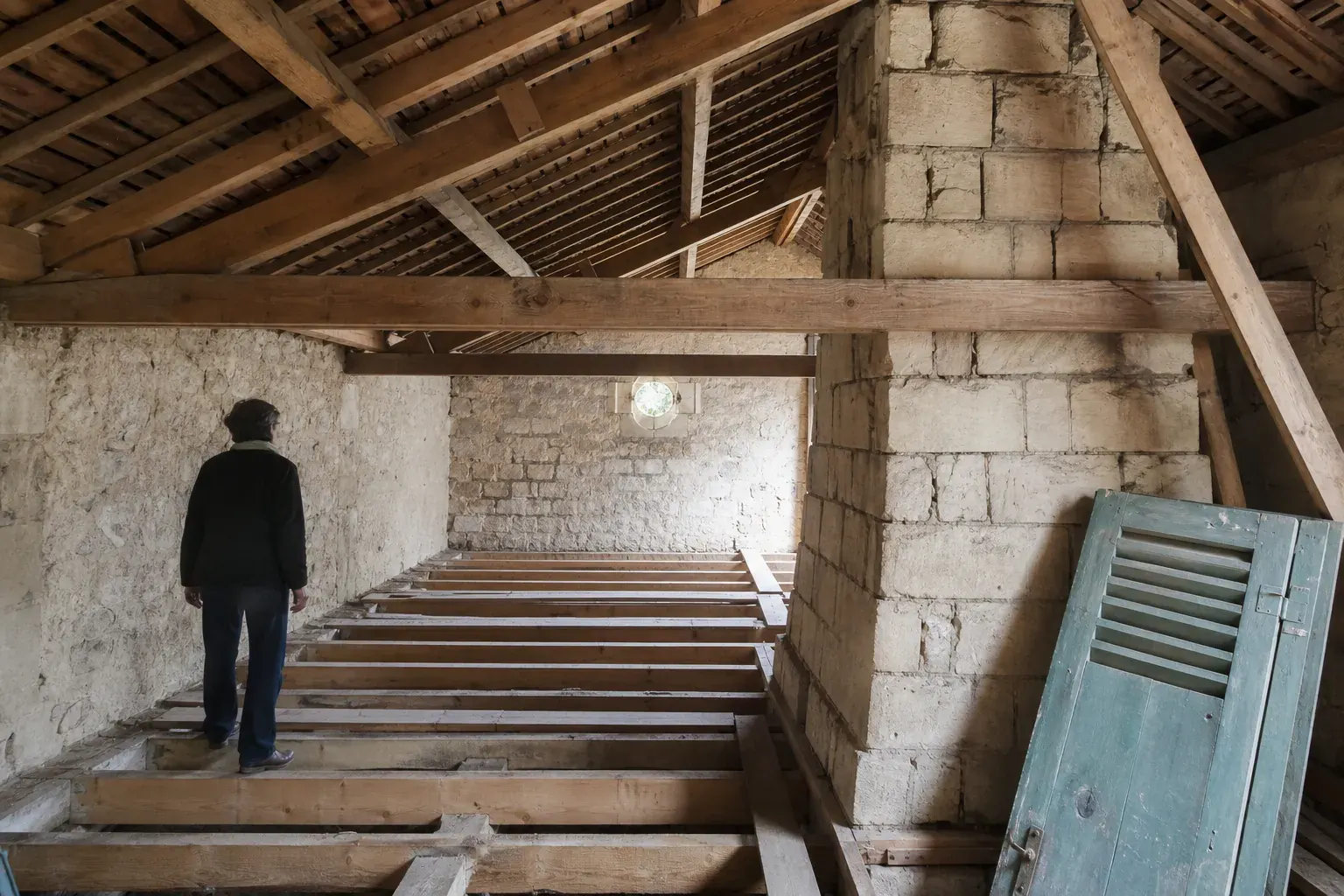 Comble perdu vide avant isolation, solives apparentes et souche de cheminée sous la lumière d’une jouée
