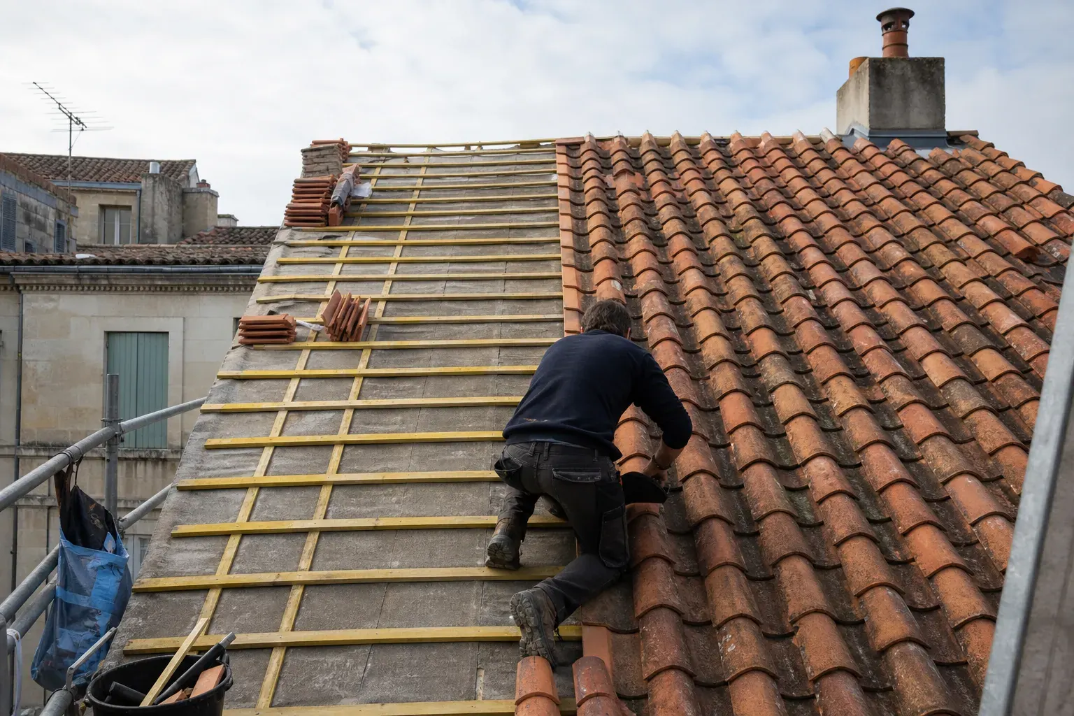 Toiture à demi reprise vue depuis l’échafaudage, un versant en tuiles neuves et l’autre encore sur liteaux nus