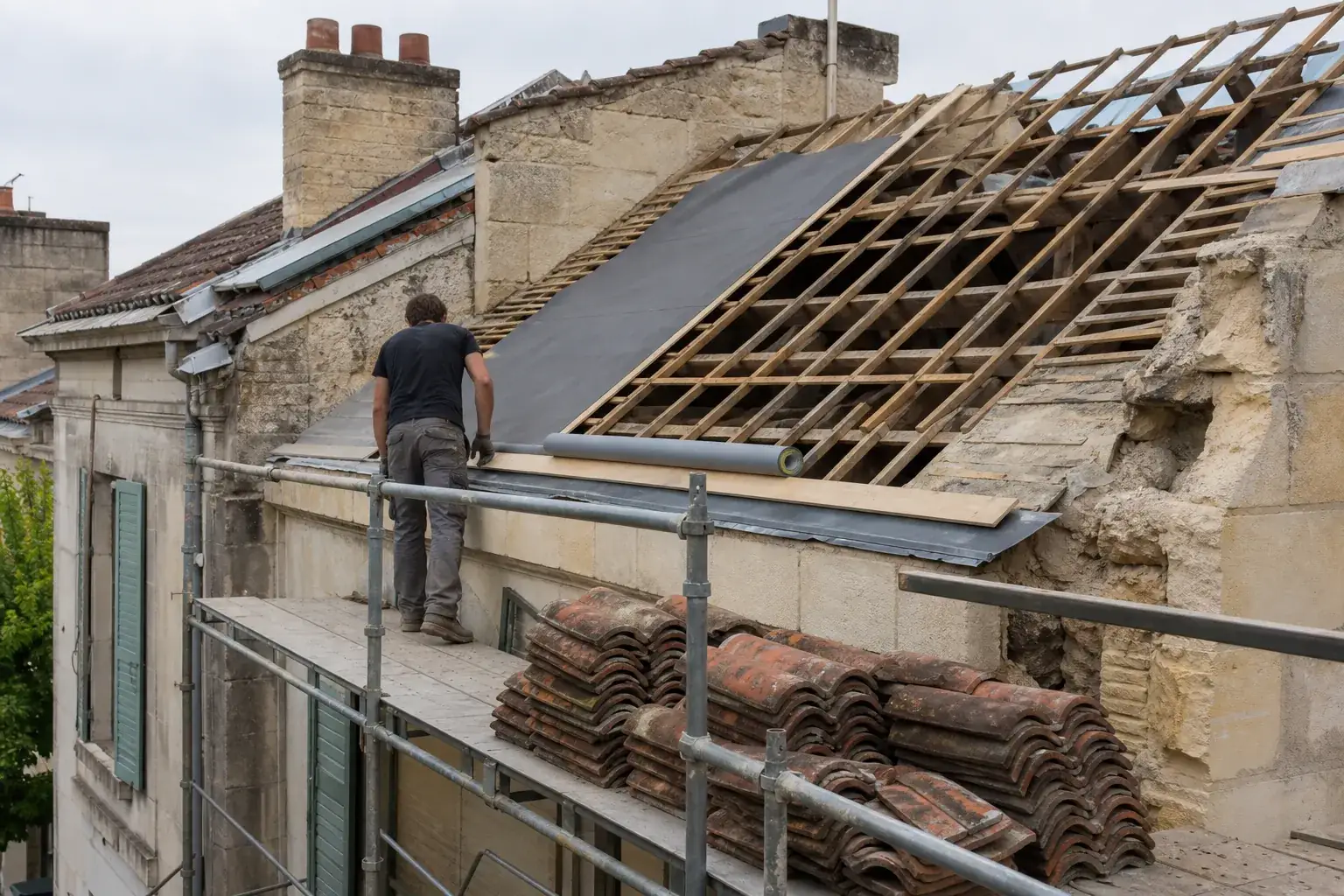 Toiture déposée jusqu’aux chevrons, écran sous-toiture à demi déroulé, tuiles récupérées empilées sur l’échafaudage
