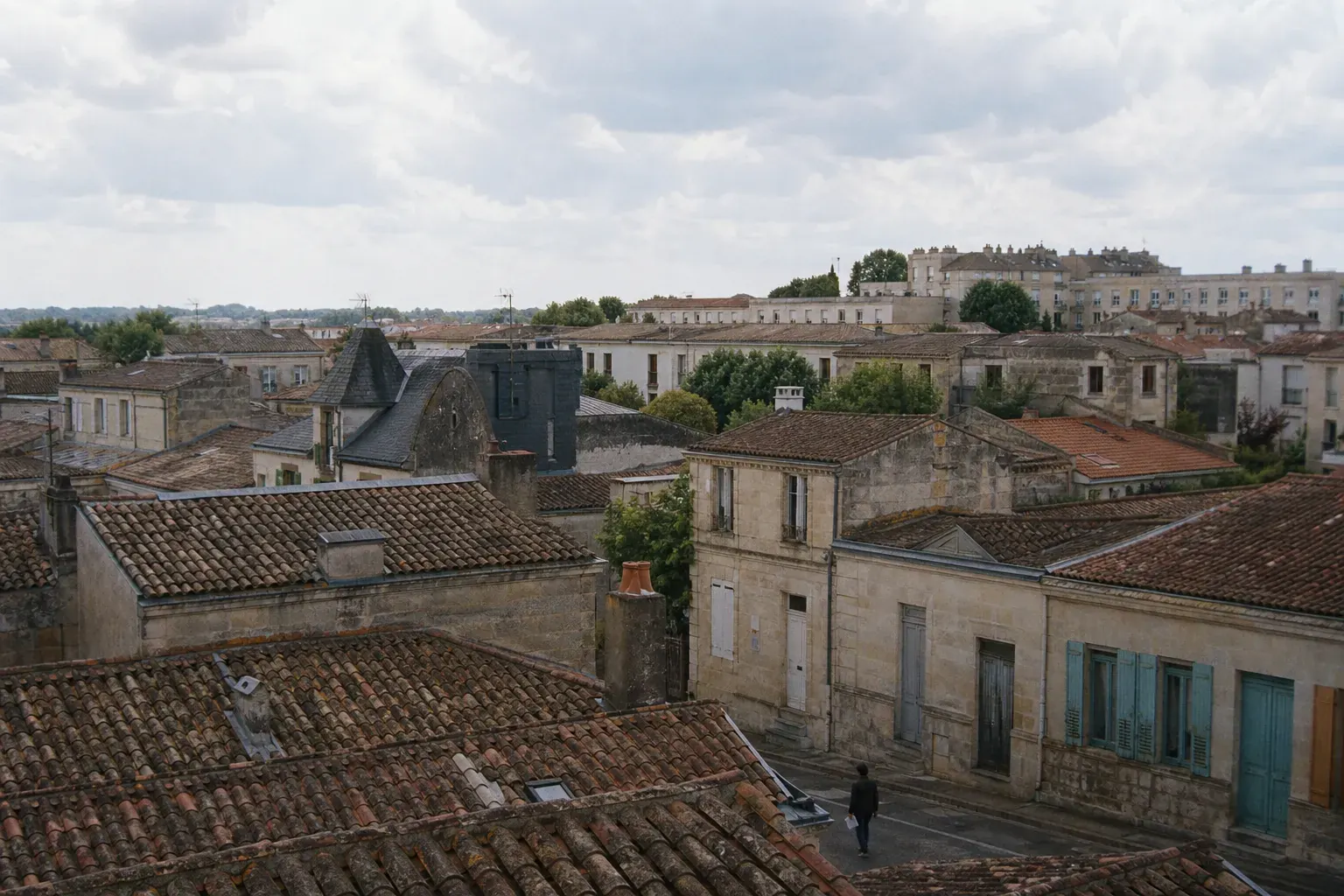 Vue large sur les toits de tuile d’un faubourg bordelais depuis une fenêtre haute, ciel atlantique dégagé